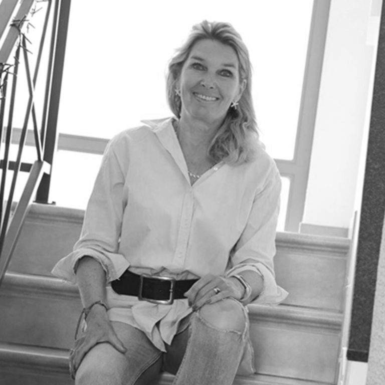 Katrin Marnitz Frau sitzt auf einer Treppe und lächelt, trägt ein weißes Hemd und Jeans.