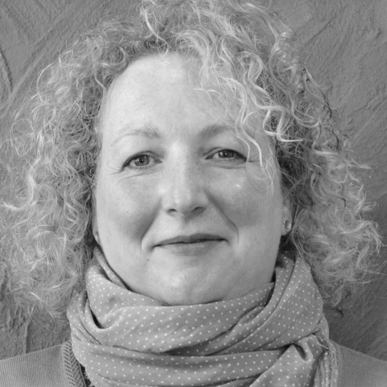 Anke Walther Frau mit lockigem, schulterlangem Haar und einem Schal, freundlicher Ausdruck.