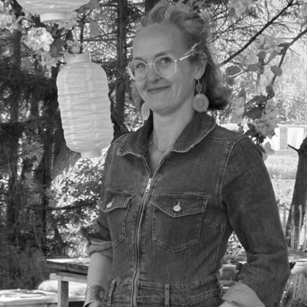 Petra Lubiger Junge Frau in Jeansjacke mit Brille und großen Ohrringen, lächelt im Freien.